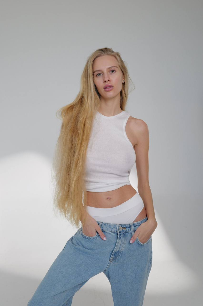 Natural blonde fashion model with waist-length platinum hair wearing a fitted white crop top and relaxed light blue jeans, clean white studio background, effortless luxury style, Scandinavian minimalism, premium fashion editorial, ultra-realistic commercial photography