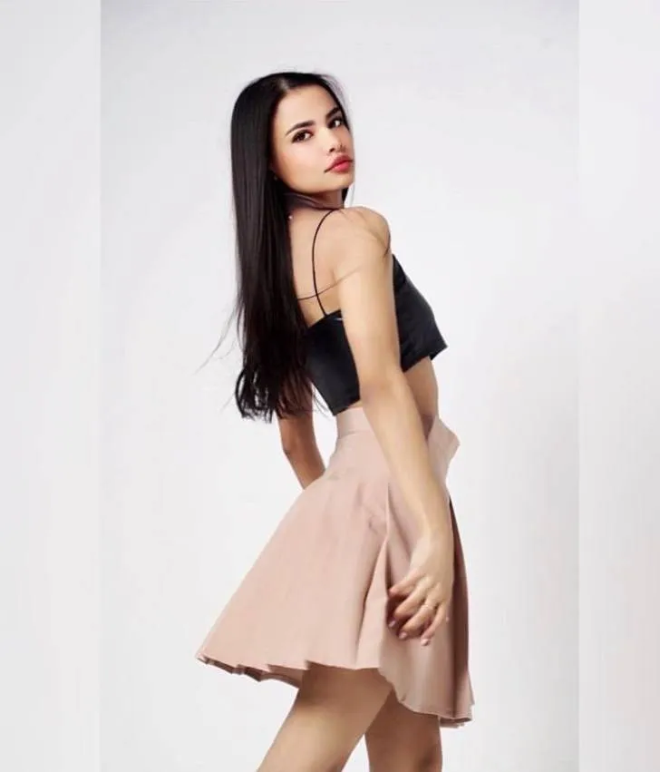beautiful slim brunette woman wearing black satin crop top and blush pink flared mini skirt, clean white studio background, elegant fashion photoshoot, full body pose