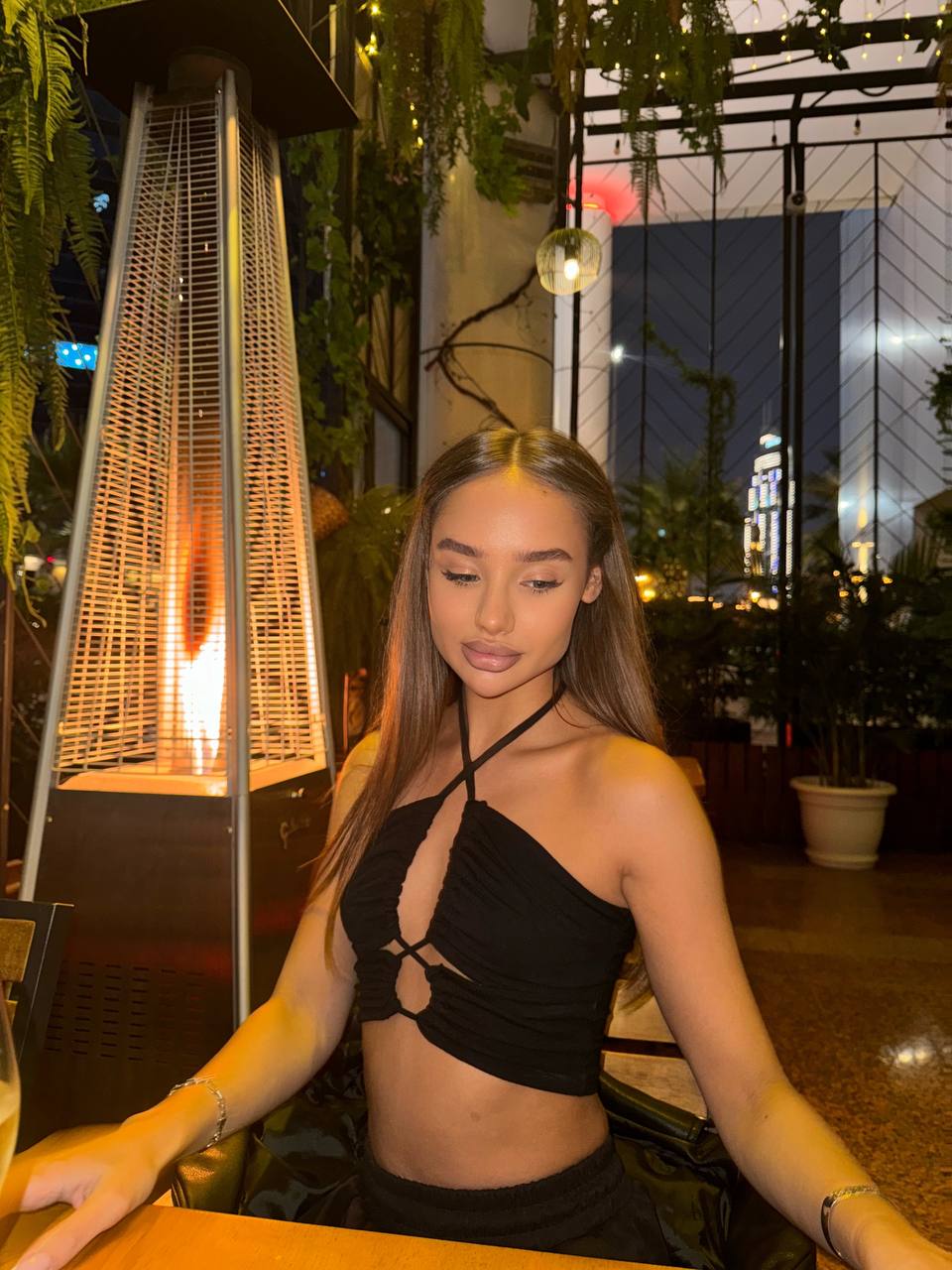Elegant brunette model in a black crop top posing at a luxury restaurant with warm evening lighting.