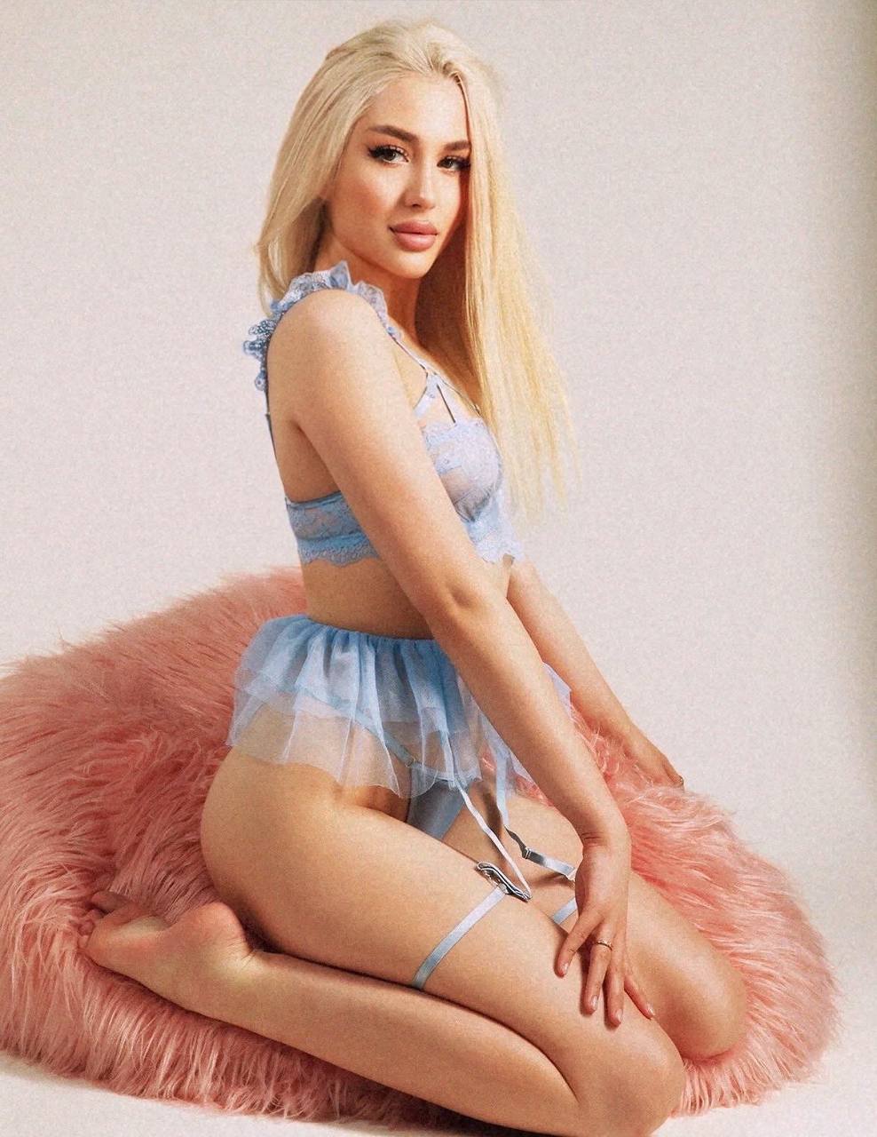 beautiful blonde woman in blue lace lingerie set with garter belt posing on pink faux fur chair