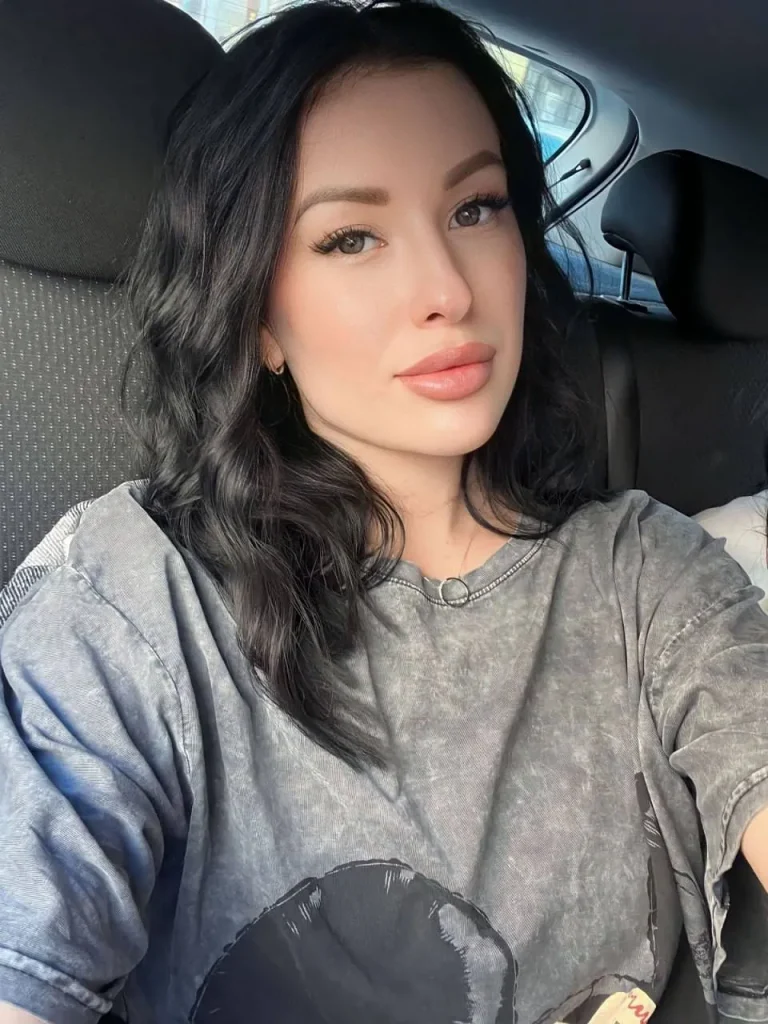 attractive woman with wavy black hair taking selfie in casual gray oversized t shirt