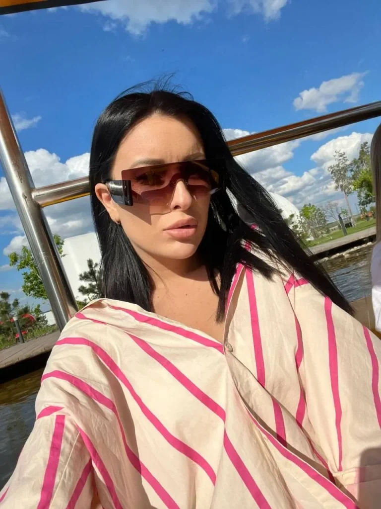 stylish brunette woman wearing oversized striped shirt and futuristic sunglasses on luxury yacht