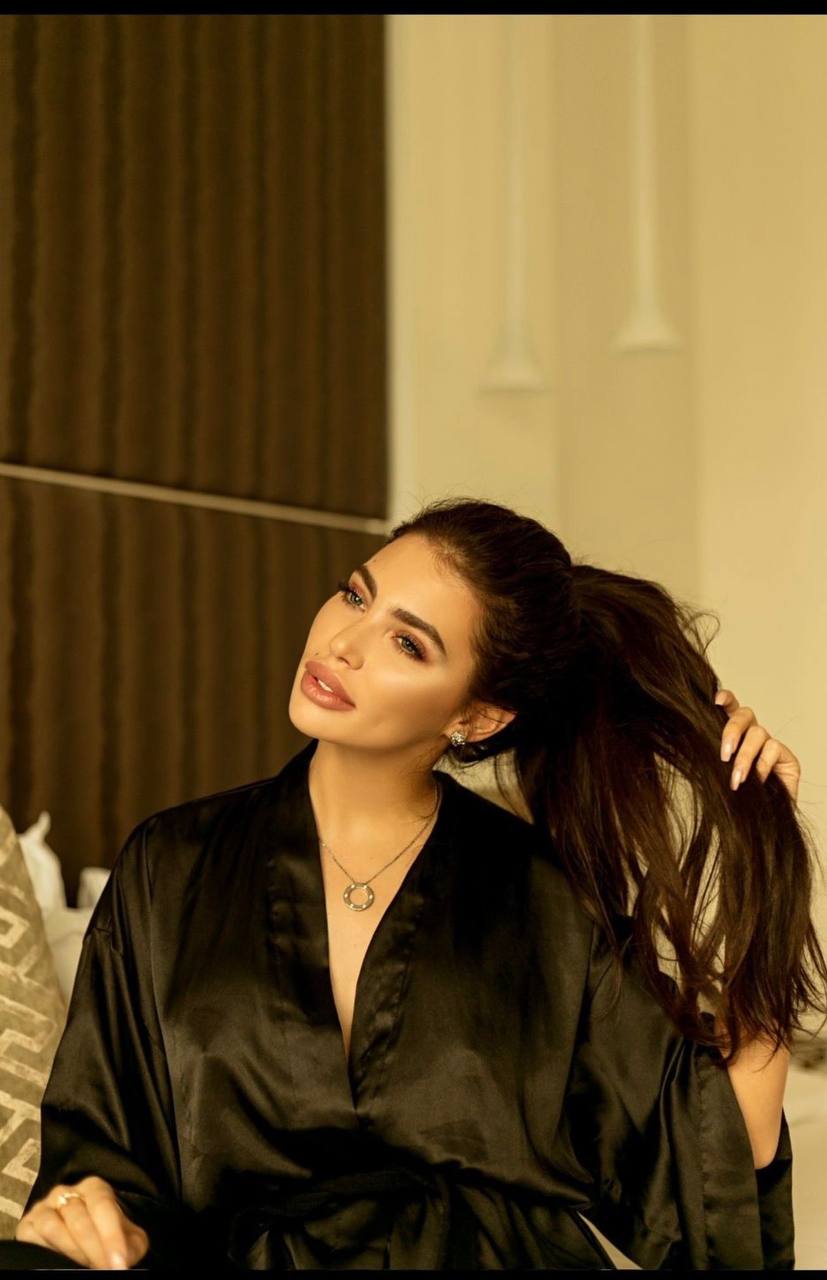 Beautiful fashion model with long dark brown hair tied in a high ponytail, wearing a black silk robe inside a luxurious hotel suite, warm golden lighting, expensive interior, sophisticated feminine look, luxury lifestyle editorial, photorealistic.