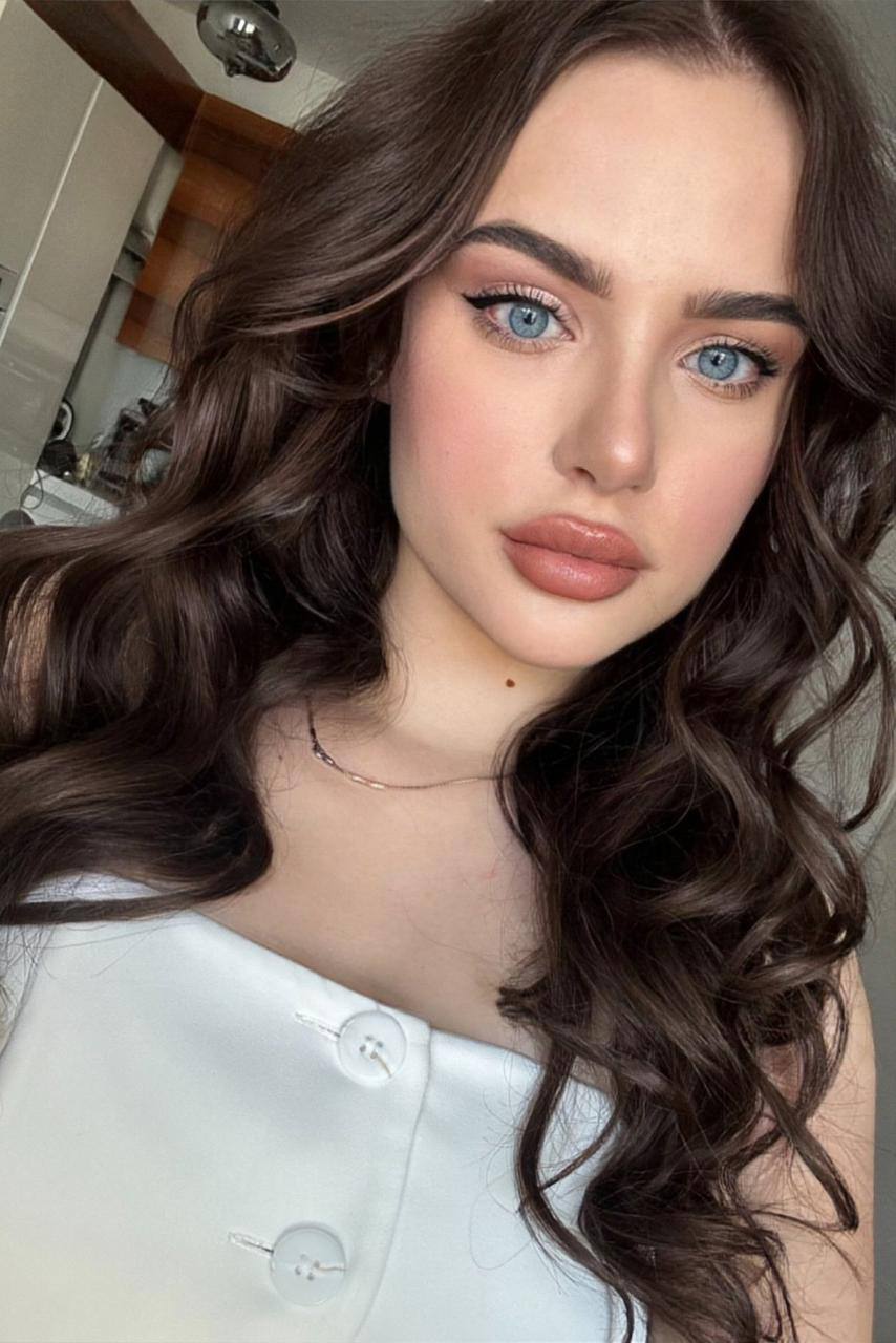 Ultra realistic beauty portrait of a gorgeous young woman with long voluminous dark brown waves, striking blue eyes, flawless porcelain skin and natural glamorous makeup, soft daylight, luxury beauty photography, highly detailed, photorealistic.