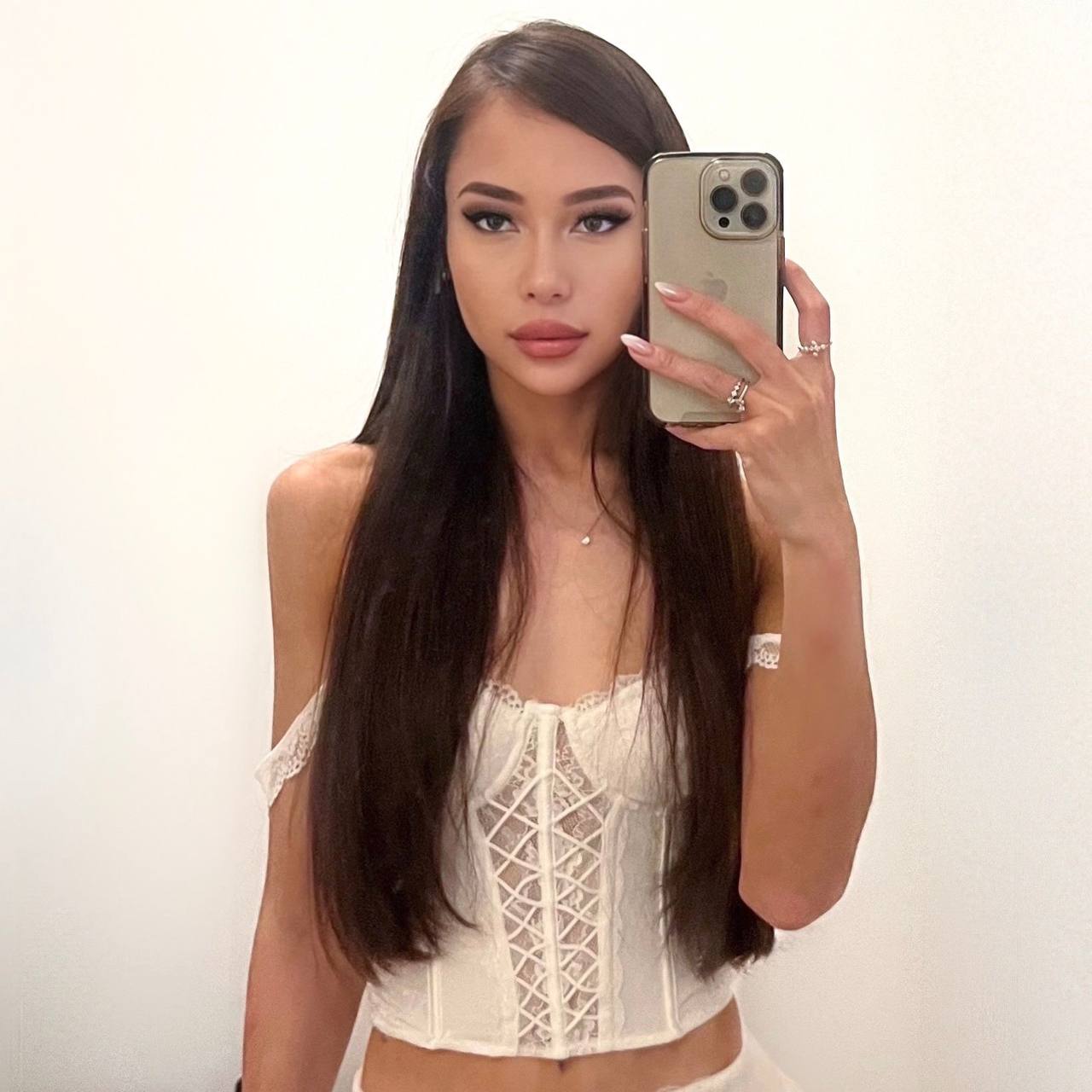 Beautiful brunette woman taking a mirror selfie wearing a white lace corset top, long straight hair, luxury beauty portrait, minimalist background, premium fashion photography