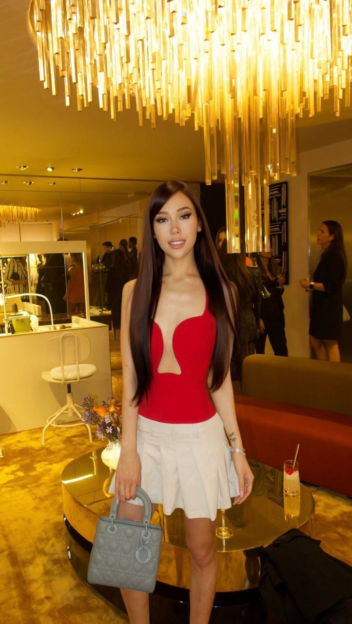 Beautiful brunette model wearing a red designer top and white mini skirt at a luxury fashion event, elegant handbag, premium lifestyle photography, high-end interior