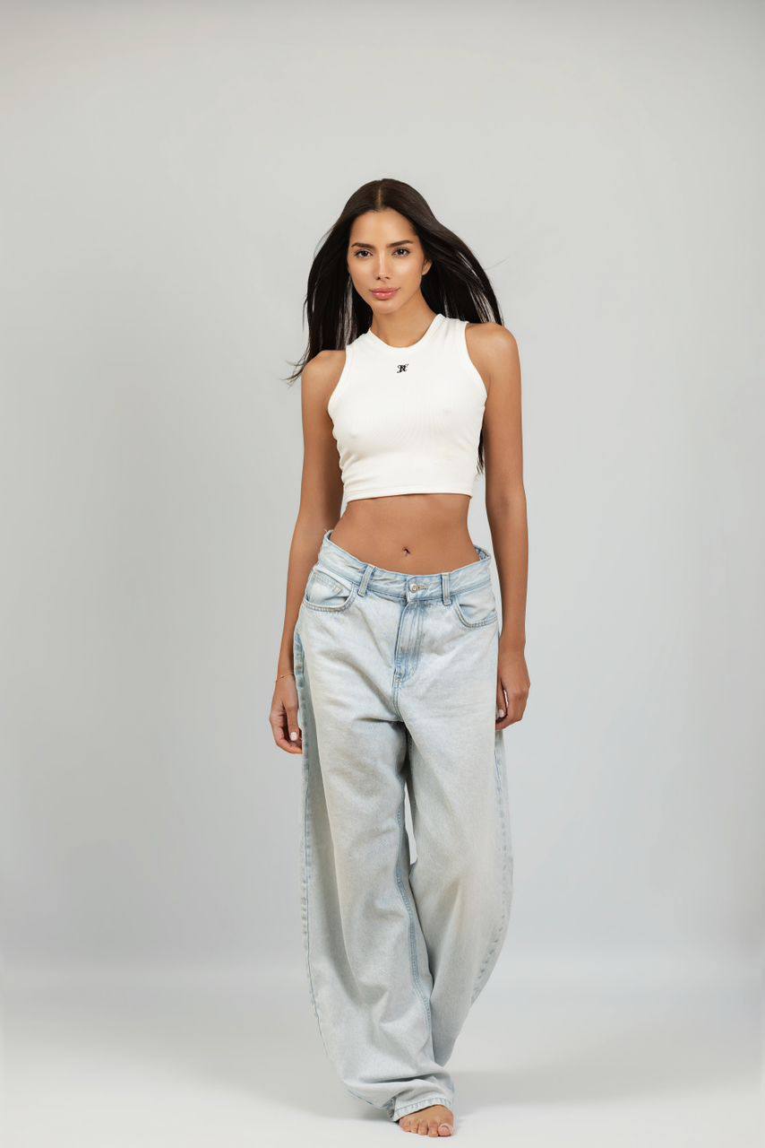 Beautiful brunette escort model wearing a white crop top and oversized jeans in a studio portrait