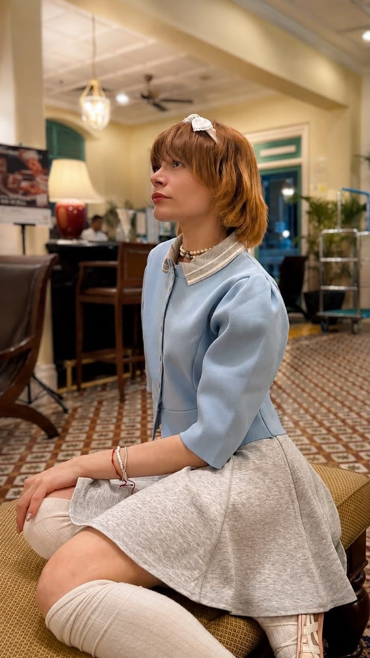 Side profile of a young blonde woman wearing a pastel blue dress with pearl accessories in an elegant hotel lobby