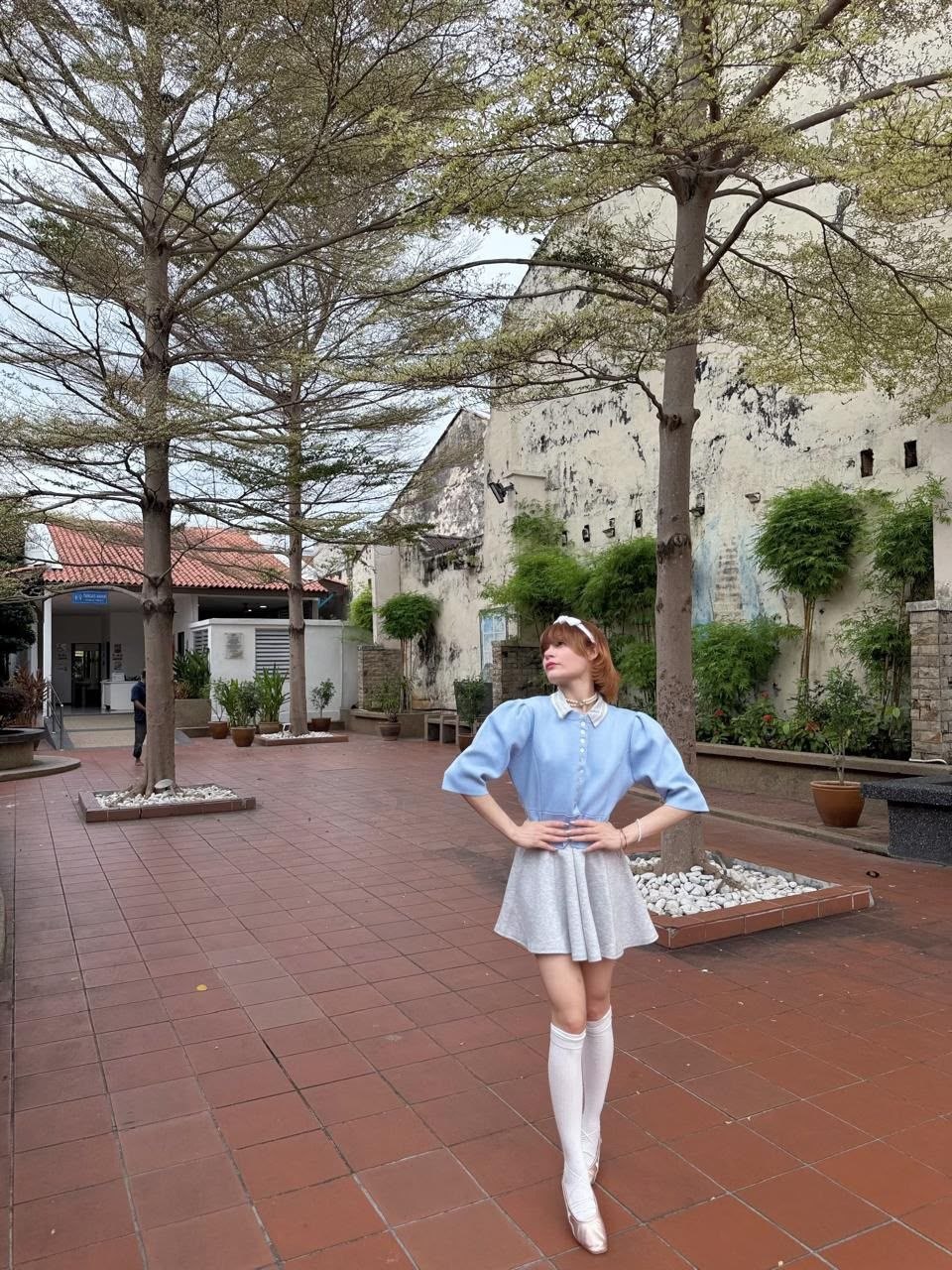 Young blonde woman posing outdoors in a pastel blue dress with knee high socks in a charming courtyard setting