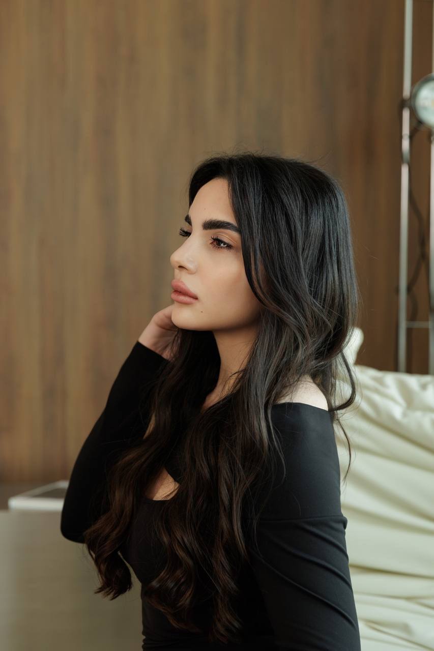 Side profile portrait of a beautiful VIP escort model with long dark hair wearing a black elegant dress