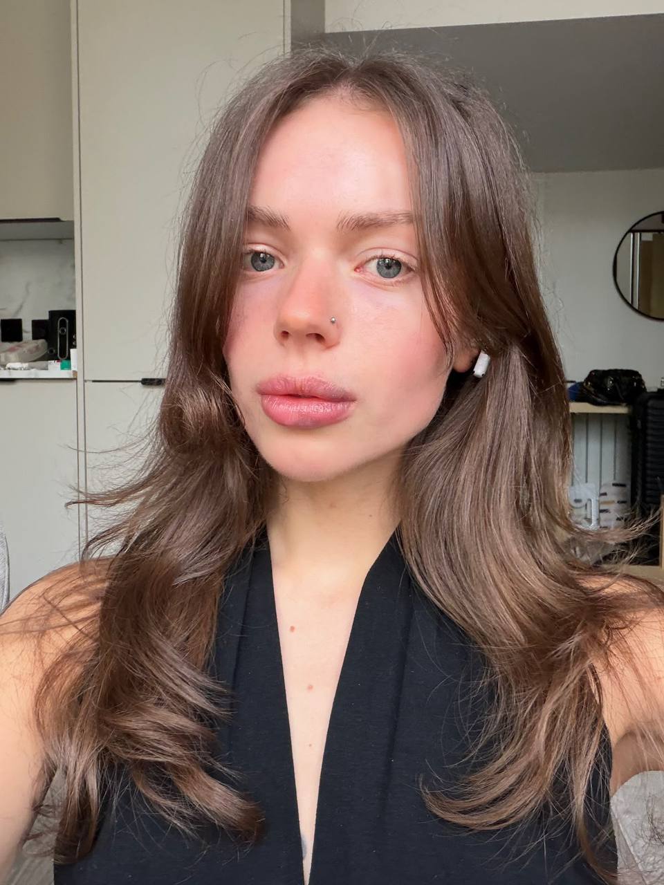 Close-up portrait of a beautiful brunette woman with blue eyes, natural makeup and wavy brown hair in soft daylight inside a modern apartment