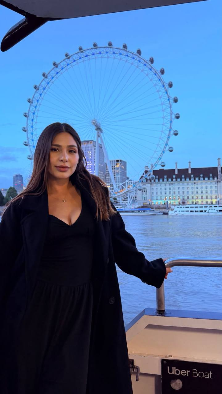 Elegant brunette fashion model wearing a black dress near the London Eye at blue hour, luxury travel editorial, cinematic city lights, premium lifestyle photography, sophisticated European fashion