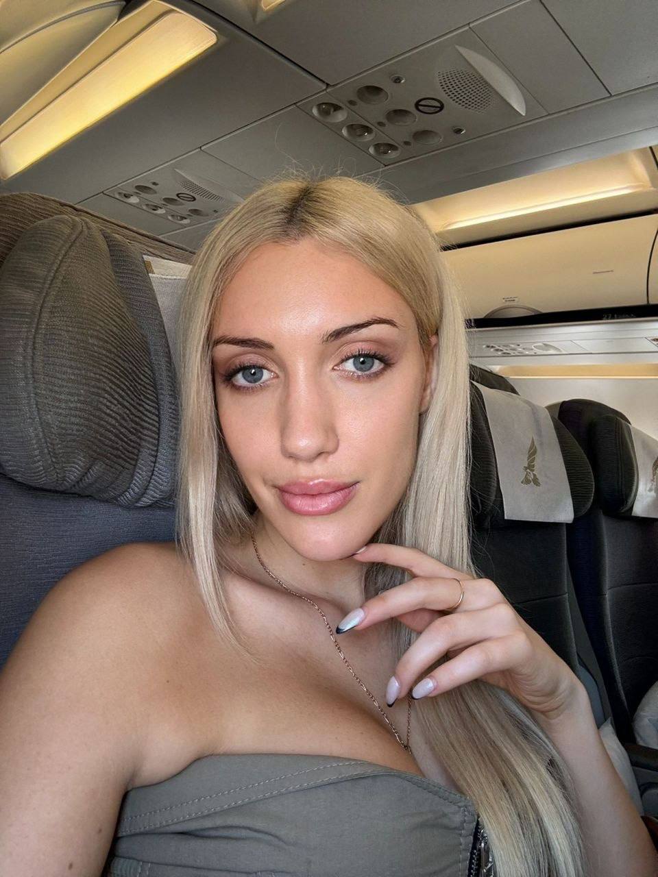 beautiful blonde woman taking selfie on airplane cabin