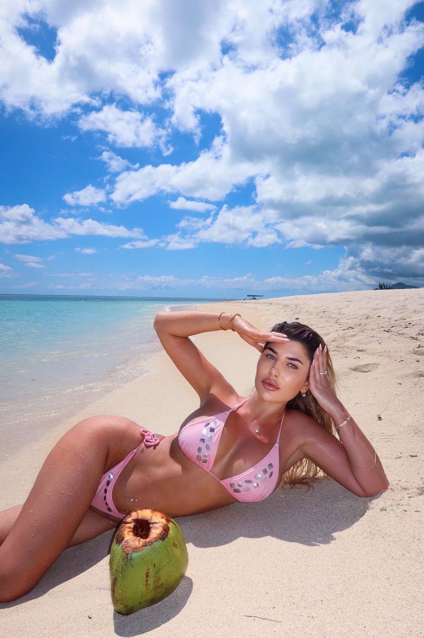 Luxury blonde escort model relaxing on a tropical beach wearing a pink bikini under the summer sun
