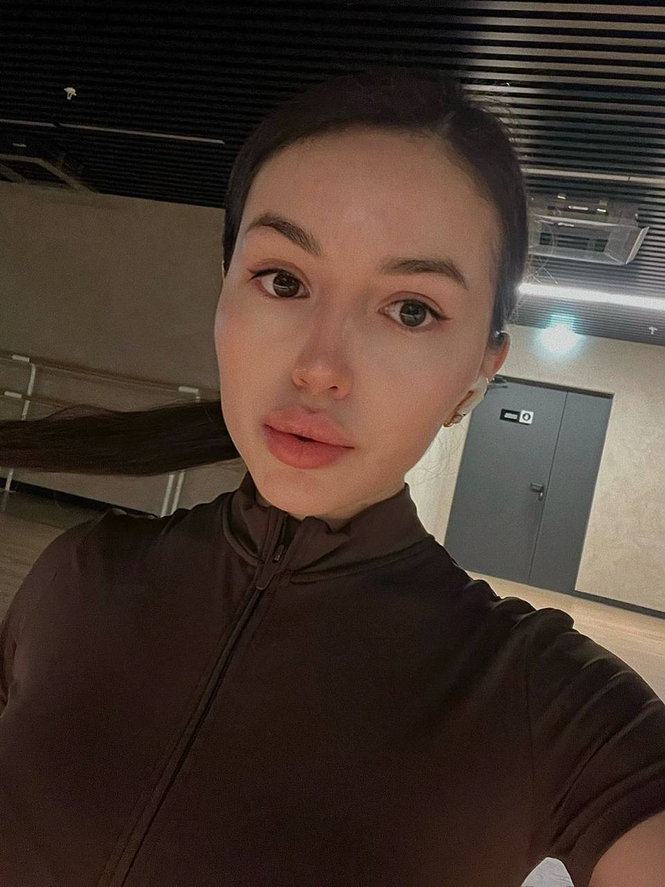 Beautiful Asian woman taking a natural indoor selfie wearing a black athletic outfit with minimal makeup.
