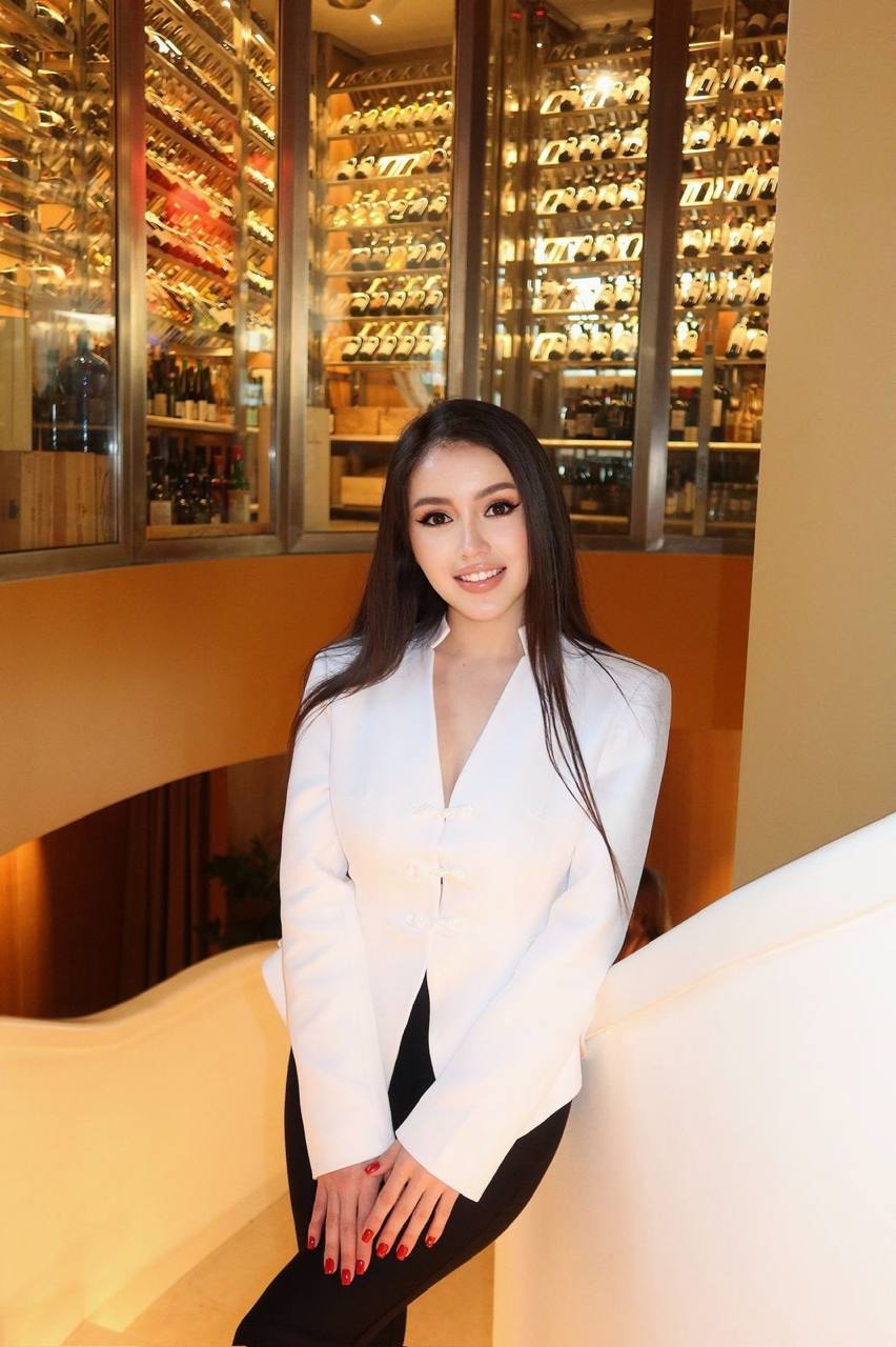 Elegant Asian fashion model wearing a white blazer posing inside a modern luxury restaurant.