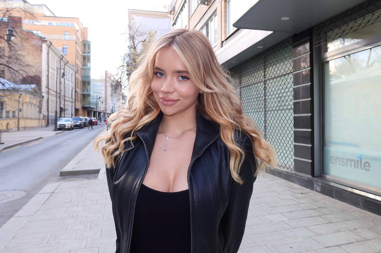 Stylish blonde luxury model walking through a European city wearing a fitted black leather jacket and elegant makeup, premium street fashion