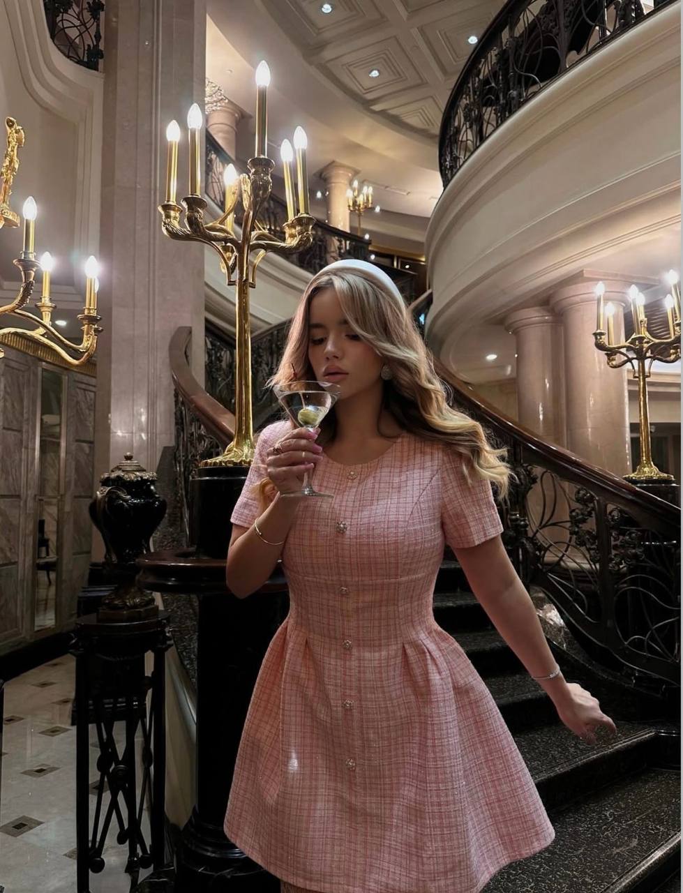 Elegant blonde VIP escort model wearing a classy pink designer dress inside a five-star hotel lobby, luxury lifestyle photography