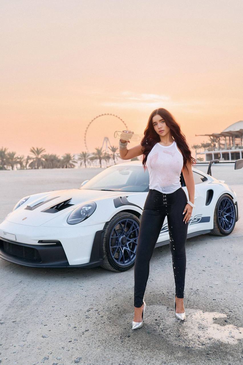 Luxury brunette fashion model posing beside a white sports car at sunset in Dubai, glamorous luxury lifestyle photoshoot