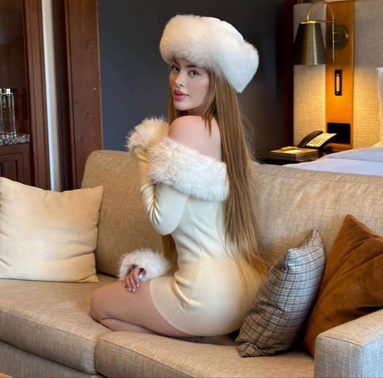 elegant woman with long auburn hair wearing white fur dress and matching winter hat indoors