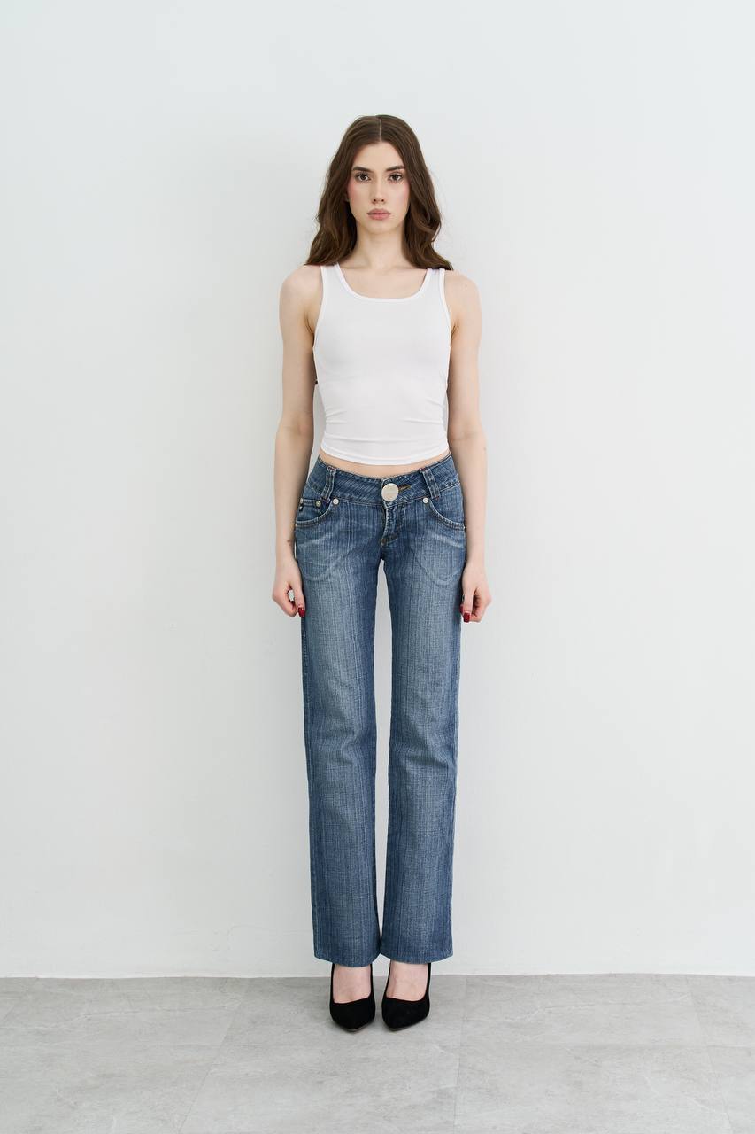 Ultra realistic full body portrait of a slim brunette woman with long dark wavy hair wearing blue jeans and a white tank top, clean studio background, natural fashion photography, realistic lighting, editorial style.
