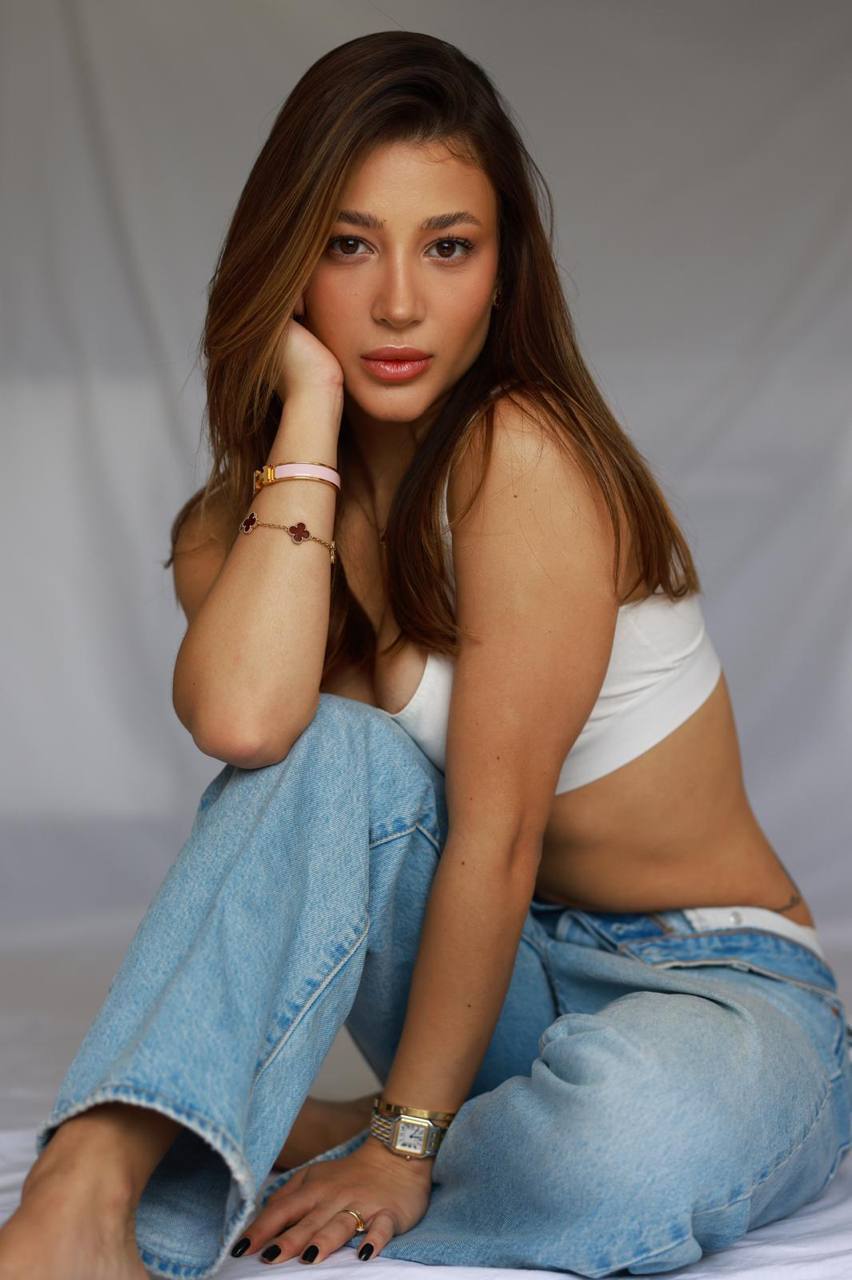 Luxury brunette model wearing a white crop top and light blue jeans, natural makeup, soft window light, clean minimalist studio, premium lifestyle portrait photography