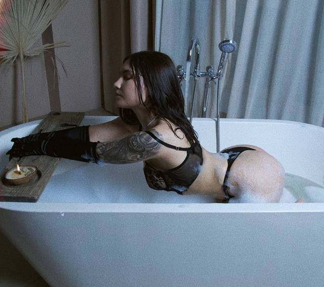 beautiful brunette woman relaxing in bubble bath wearing black lace lingerie and long black satin gloves, luxury bathroom, moody cinematic lighting
