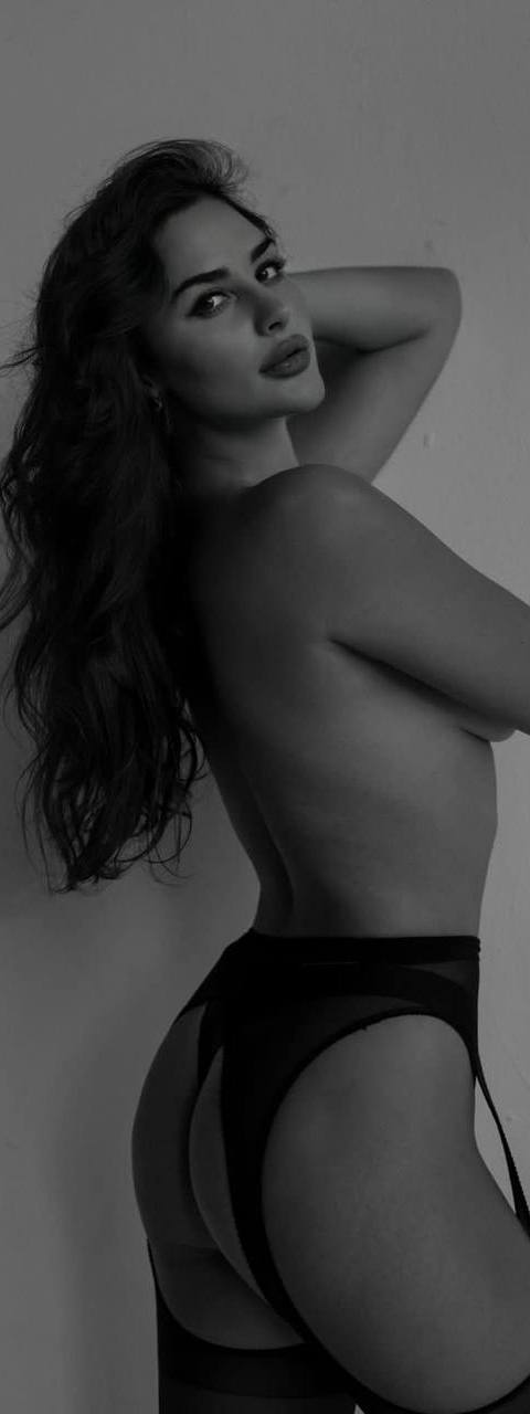 Black and white artistic boudoir portrait of a woman with long wavy hair in a garter belt and stockings posing in profile