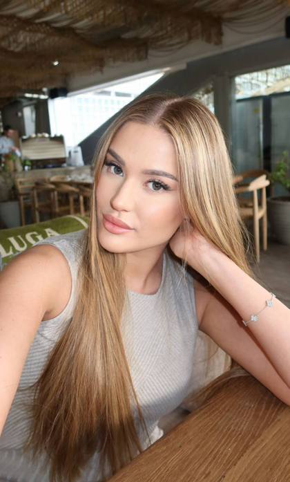 Beautiful blonde fashion model with long straight hair taking elegant selfie in modern luxury cafe wearing stylish sleeveless beige top