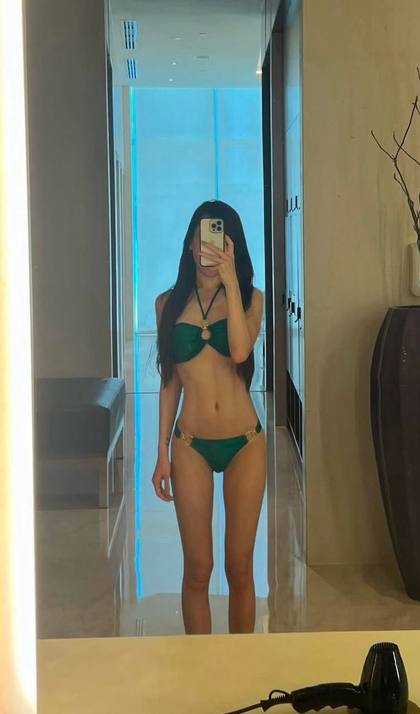 Elegant brunette fashion model taking a luxury hotel mirror selfie wearing a green designer bikini, slim figure, premium resort lifestyle photography, modern luxury interior