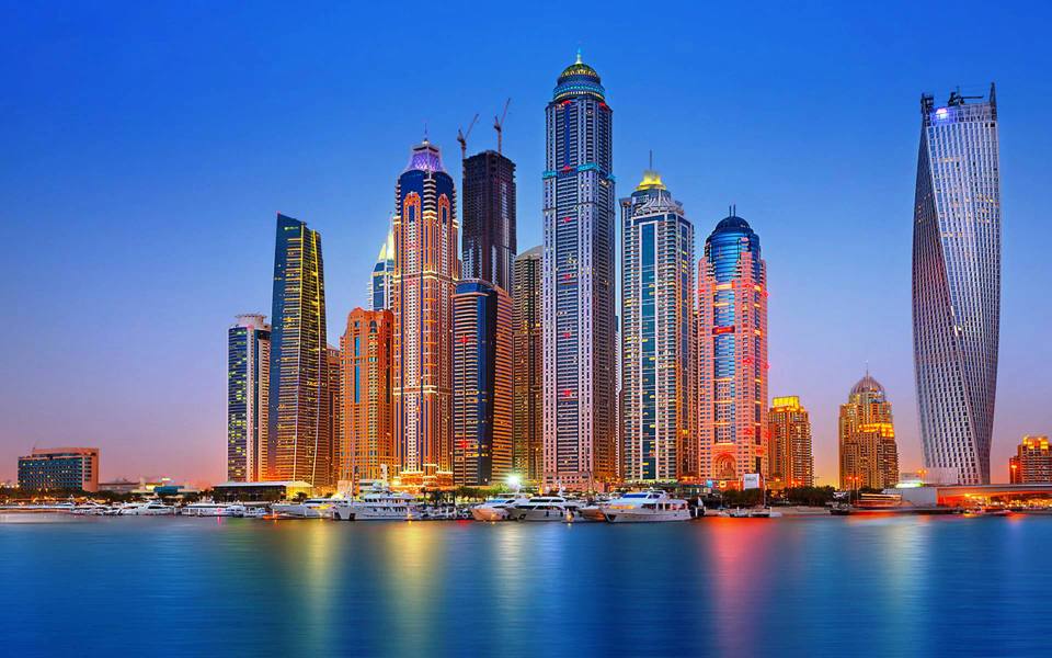 Dubai Marina skyline at dusk with illuminated skyscrapers, twisted Cayan Tower and yachts on the water