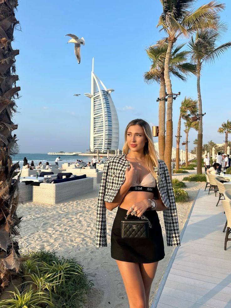 Blonde woman in houndstooth jacket and black mini skirt at a beach club with Burj Al Arab in the background, Dubai