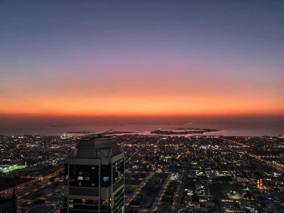 Aerial view of Dubai city lights and coastline at sunset with orange and purple sky over the Persian Gulf