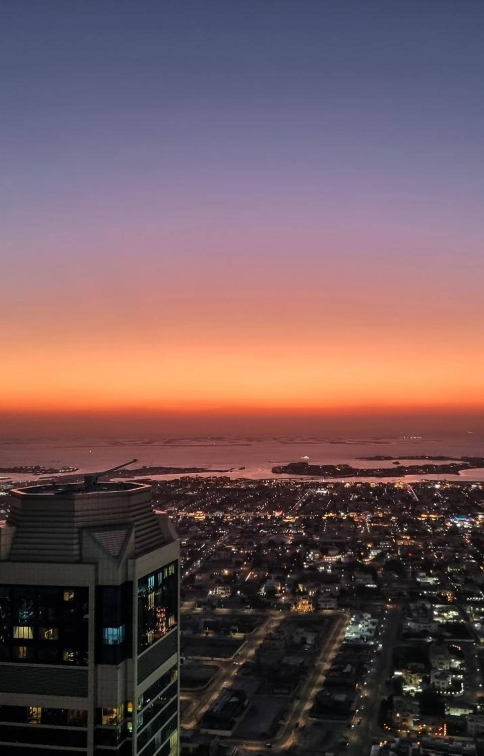 Aerial view of Dubai city lights and coastline at sunset with orange and purple sky over the Persian Gulf