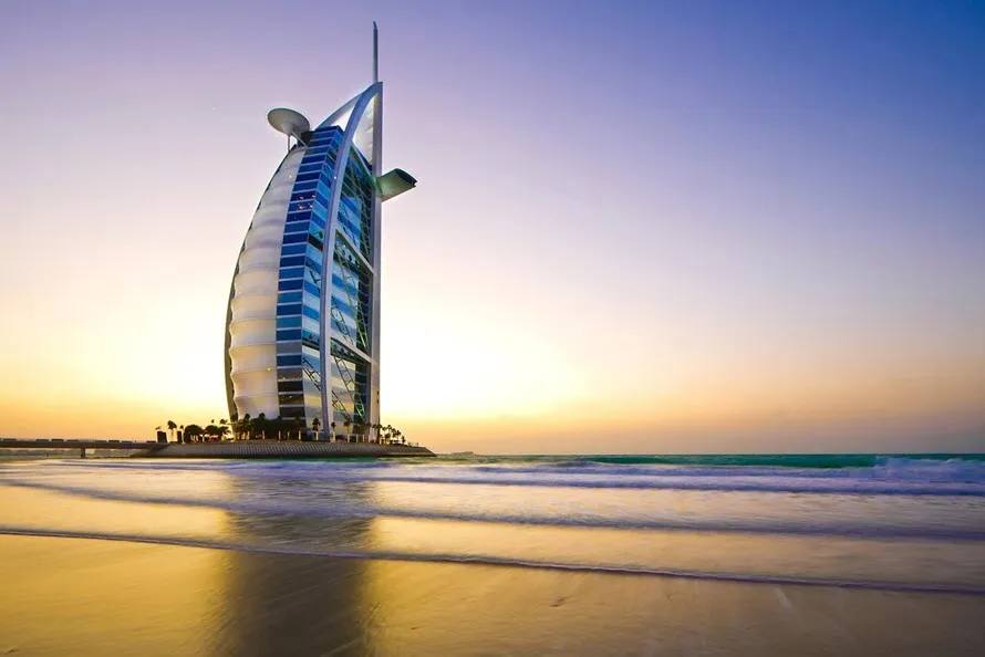 Burj Al Arab luxury hotel at sunset viewed from Jumeirah beach with waves in the foreground, Dubai