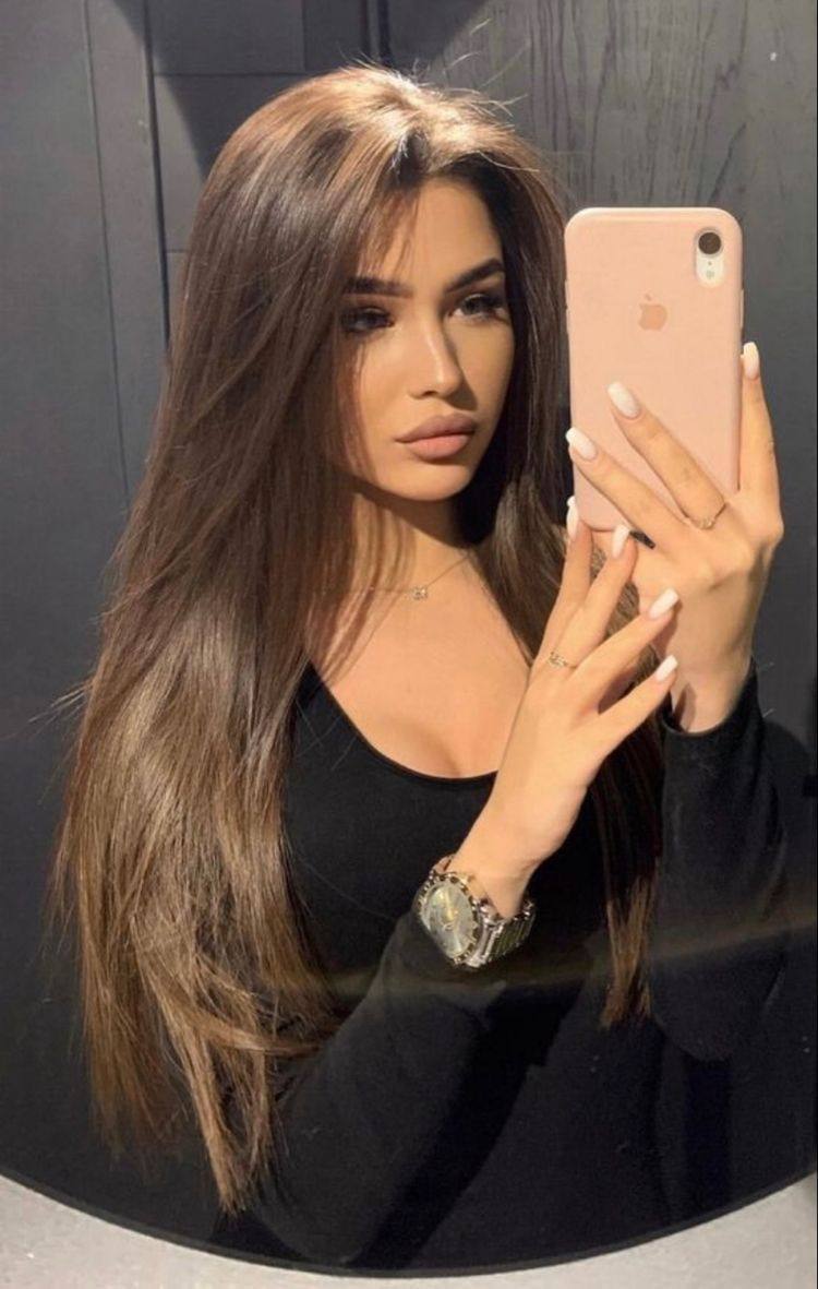 Mirror selfie of a brunette with long straight hair in a black top holding a pink phone