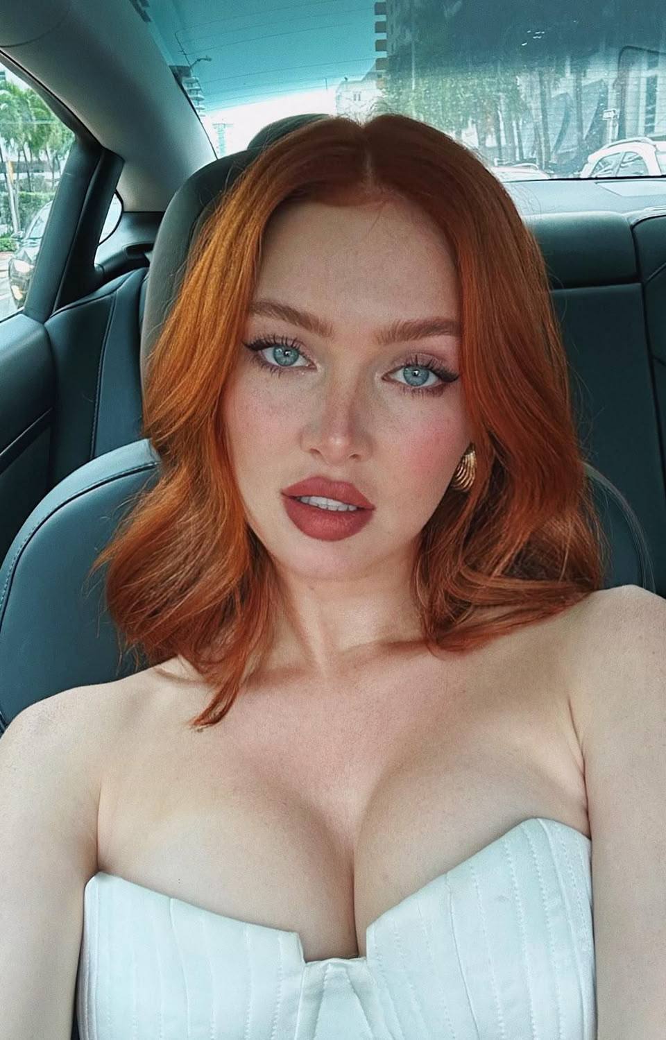 Car selfie of a redhead woman with green eyes in a white strapless corset top