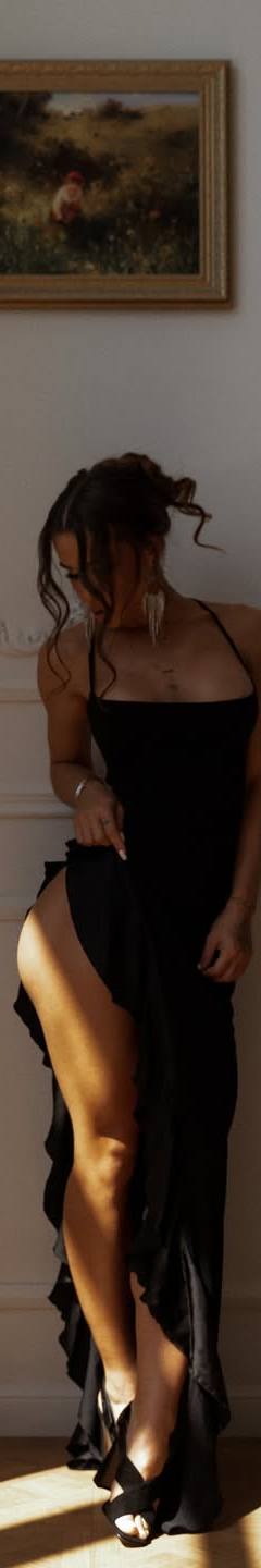 Elegant woman in a black evening dress posing in a luxurious interior with natural light