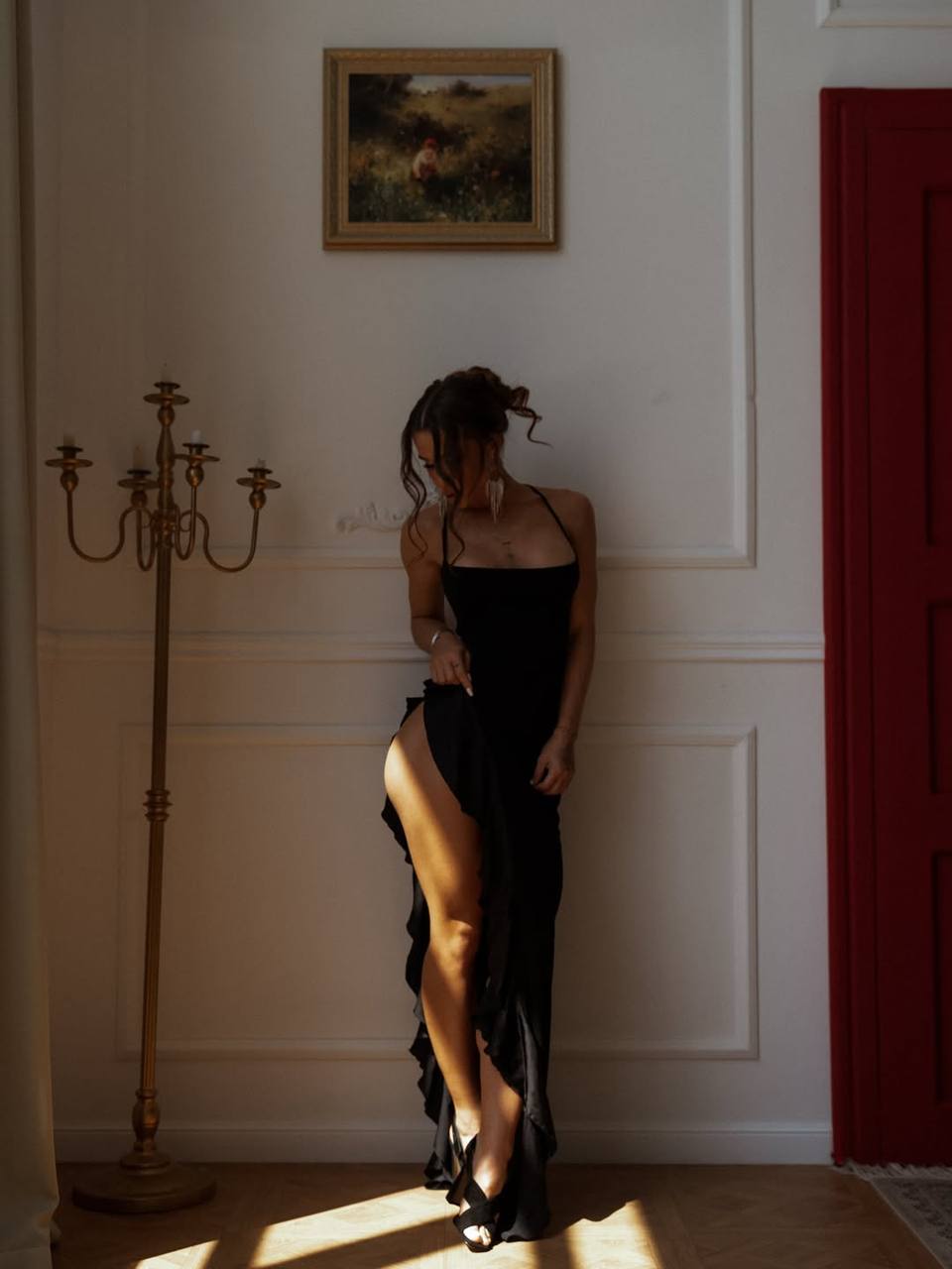 Elegant woman in a black evening dress posing in a luxurious interior with natural light