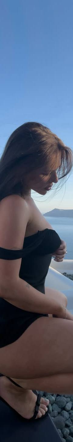 Woman in a black off-shoulder dress posing by a luxury infinity pool with a scenic sea view