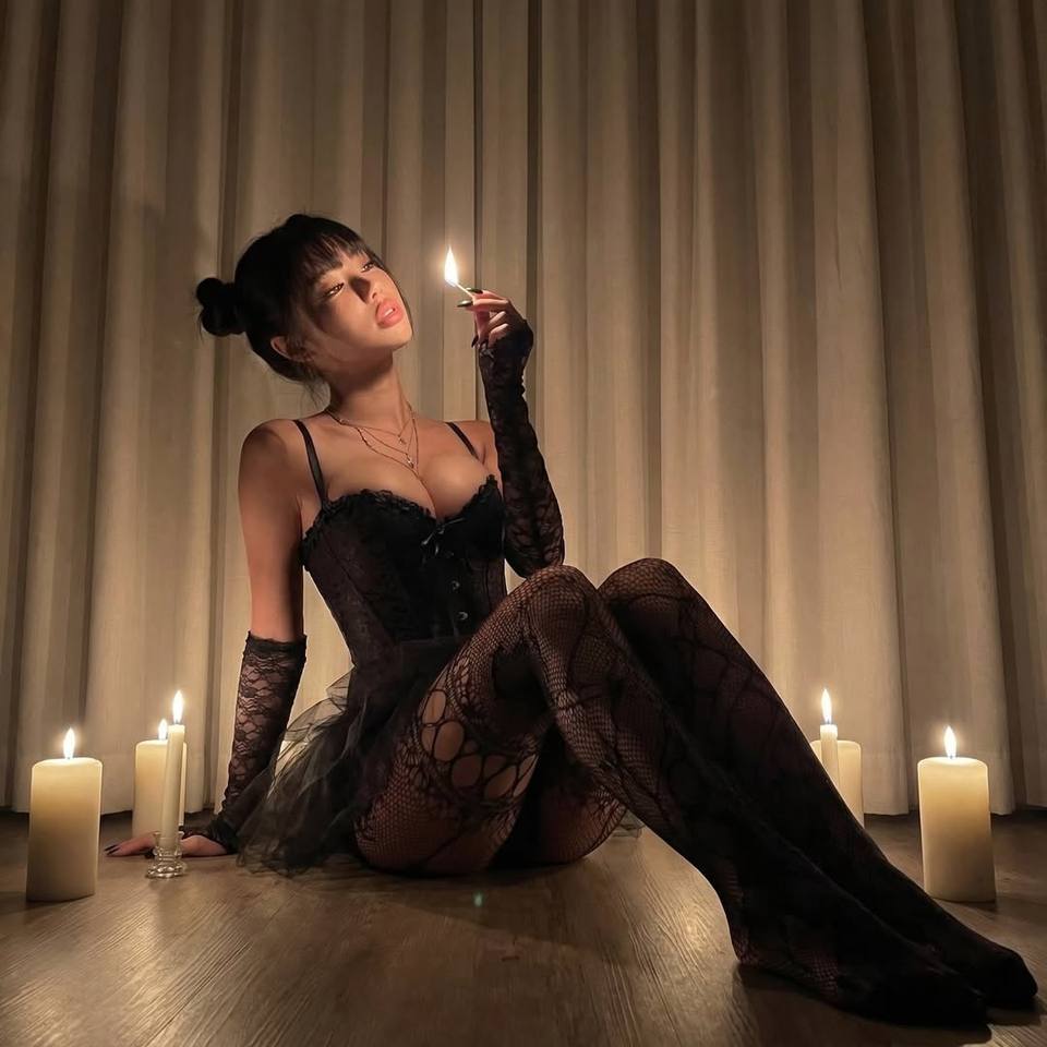 Woman in a black lace corset and stockings surrounded by candlelight in an elegant indoor setting