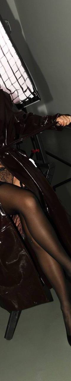 Brunette woman in black lace lingerie and a glossy trench coat posing in a professional studio photoshoot