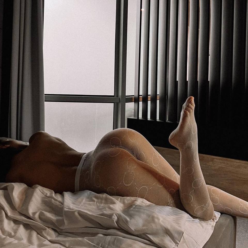 Woman wearing patterned white stockings relaxing on a bed in a modern luxury bedroom