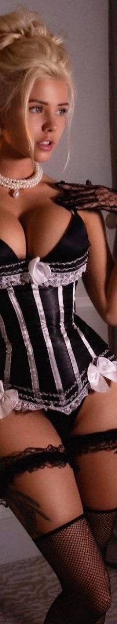 Blonde woman in an elegant black corset and fishnet stockings posing in a luxurious hotel suite