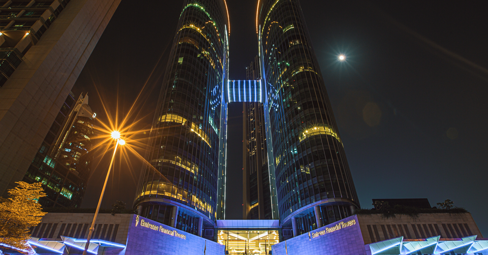 Emirates Financial Towers illuminated at night with blue and gold lights, low-angle view, DIFC Dubai