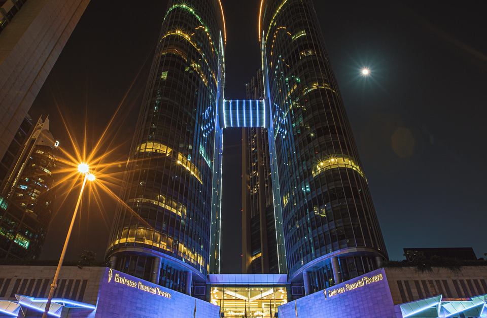 Emirates Financial Towers illuminated at night with blue and gold lights, low-angle view, DIFC Dubai