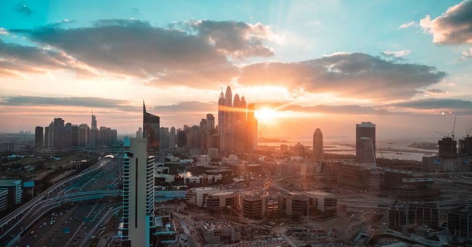 Aerial view of Dubai cityscape at sunset with sun setting behind Marina skyscrapers and busy highway below