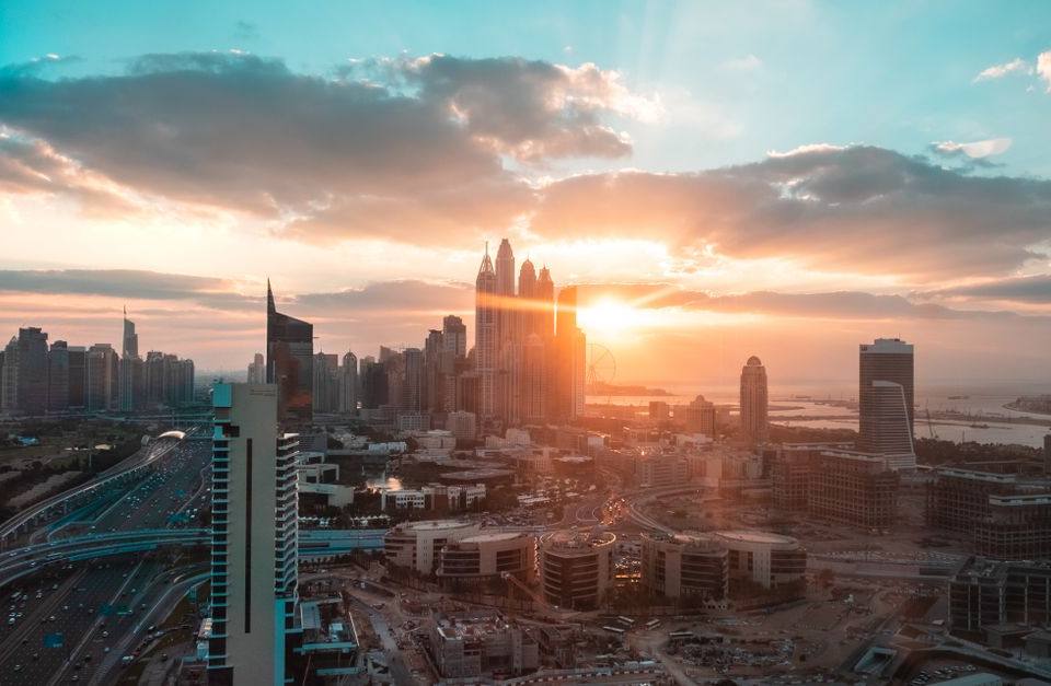 Aerial view of Dubai cityscape at sunset with sun setting behind Marina skyscrapers and busy highway below