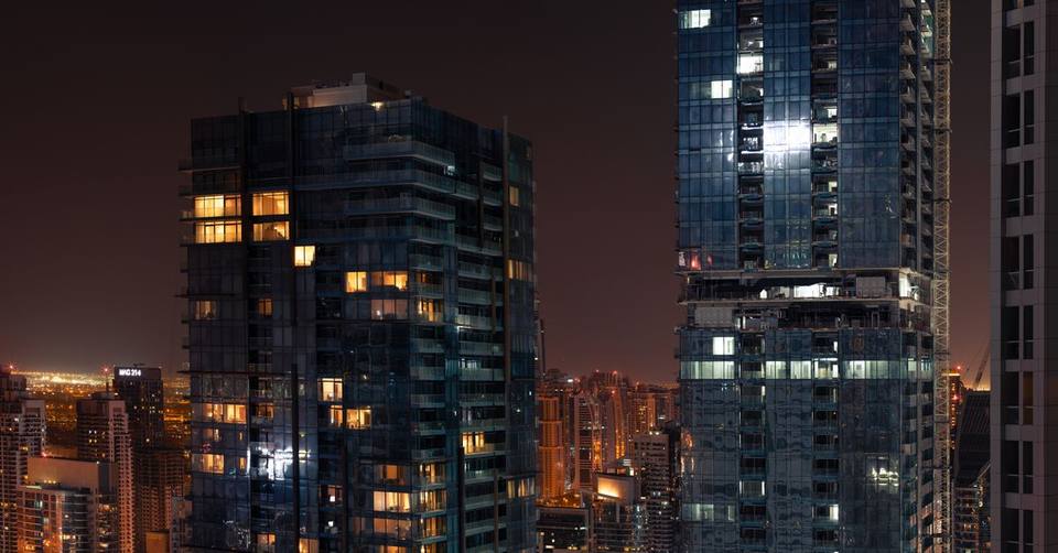 Glass high-rise towers with glowing windows at night against the Dubai city skyline