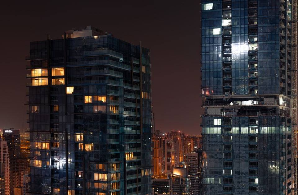 Glass high-rise towers with glowing windows at night against the Dubai city skyline